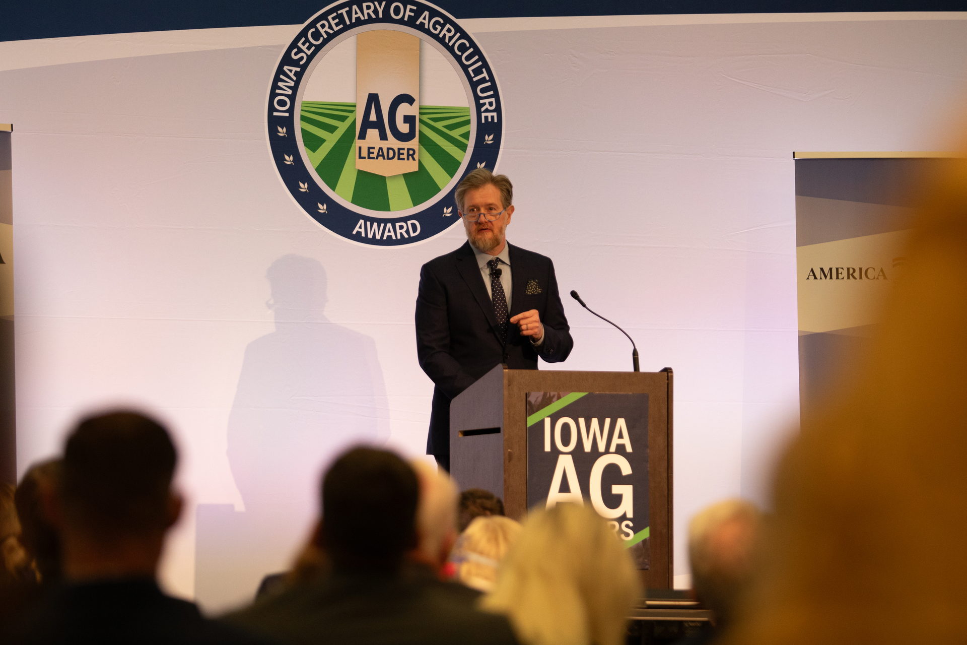 Lindsay Graham speaking at a lectern in front of an Iowa Ag Leader Award banner, with the audience in the foreground.