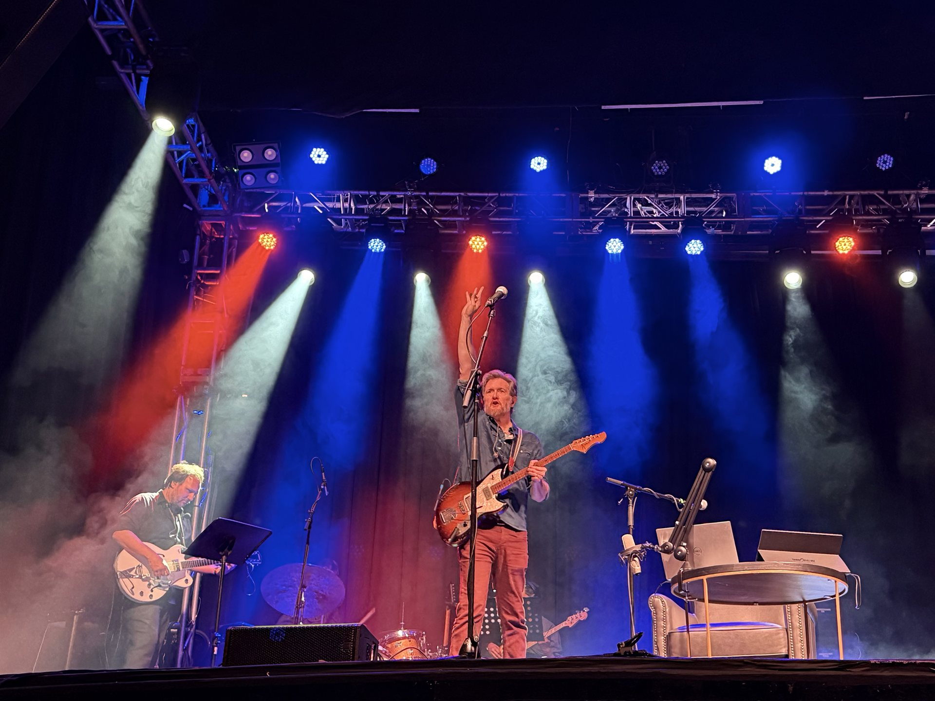 Lindsay Graham on stage with a guitar, arm raised, under red and blue concert lighting.